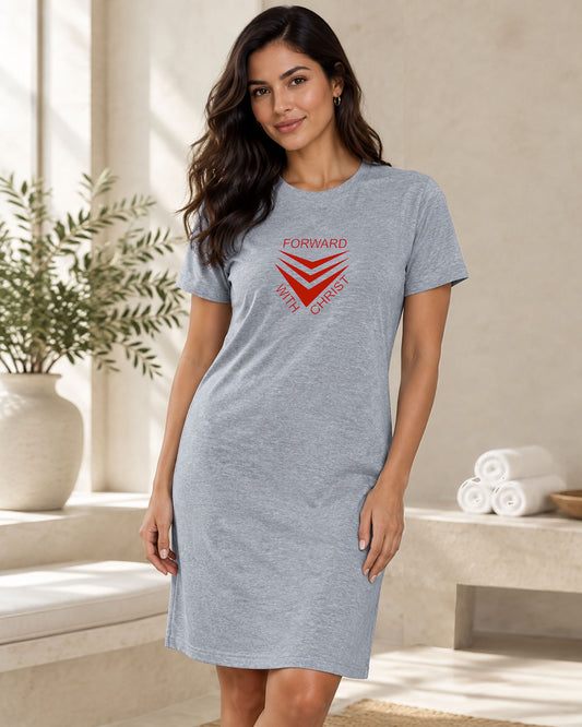 A woman modeling a heather gray short-sleeve t-shirt dress with a red chevron graphic surrounded by text 'FORWARD WITH CHRIST' on the chest, set in a bright, modern interior with a potted plant.