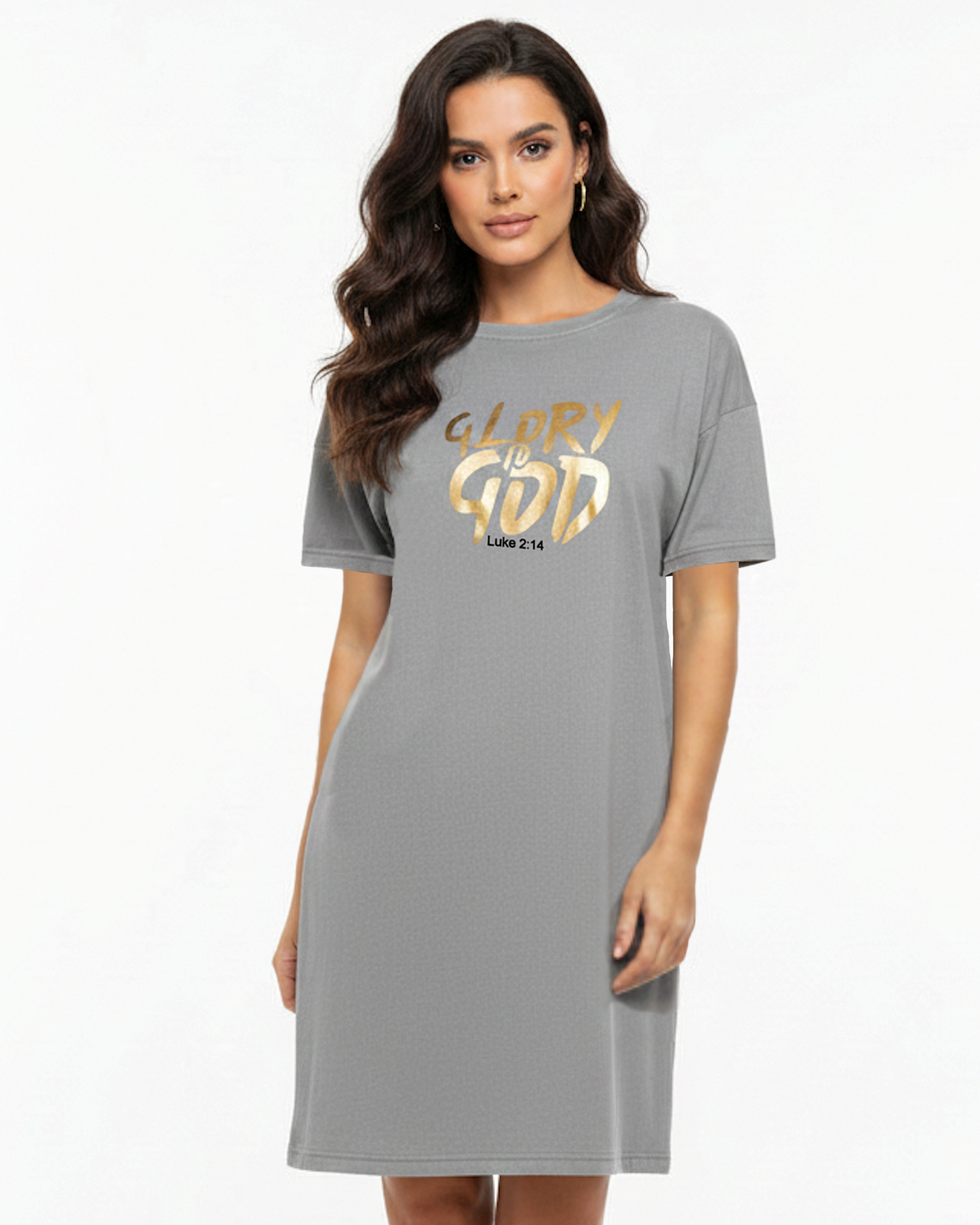 A woman modeling a grey short-sleeve t-shirt dress with a gold graphic on the chest that reads 'GLORY IS GOD' and 'Luke 2:14'.