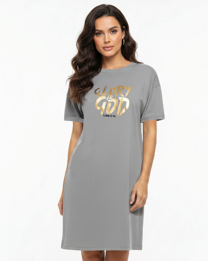 A woman modeling a grey short-sleeve t-shirt dress with a gold graphic on the chest that reads 'GLORY IS GOD' and 'Luke 2:14'.