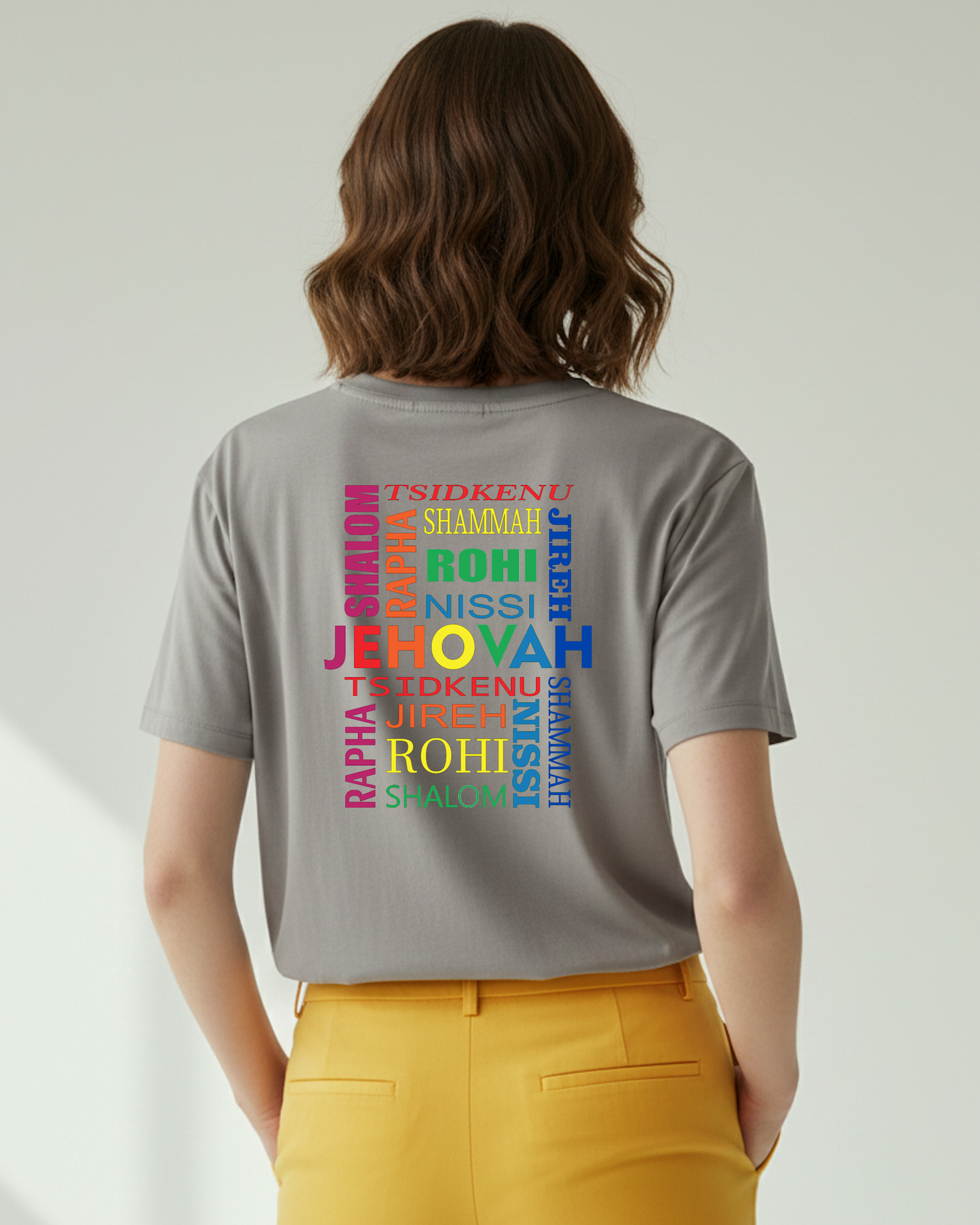Woman wearing a grey t-shirt with colorful Hebrew text design on the back, standing against a plain background.