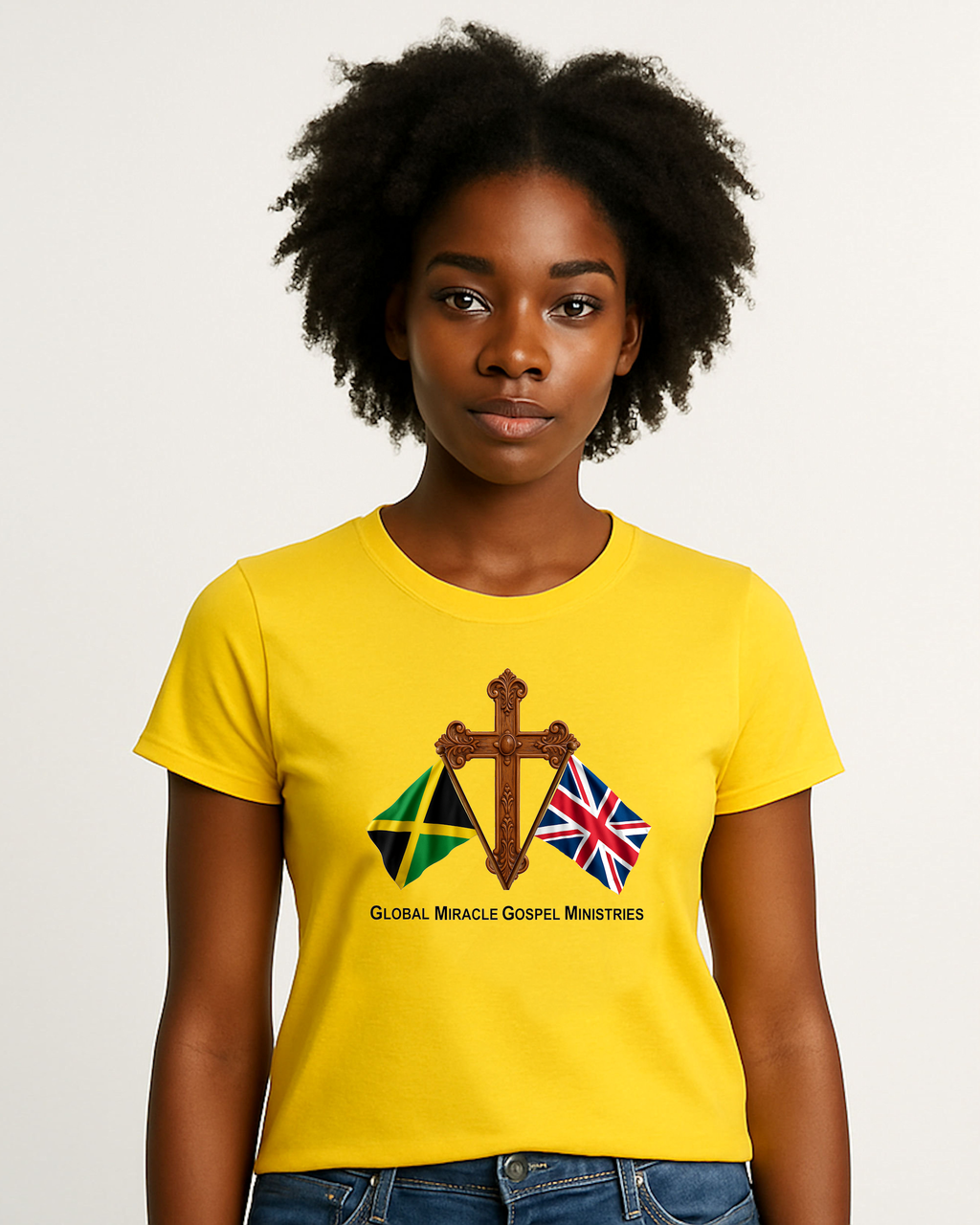 A woman wearing a yellow t-shirt with a logo comprised of a flag of Jamaica and a flag of Great Britain in front of a wooden cross and black text, "Global Miracle Gospel Ministries" standing against a white background.
