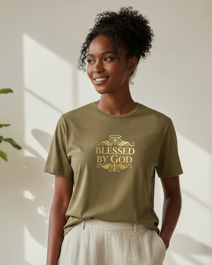 Woman wearing a khaki t-shirt with gold 'Blessed by God' text logo on the front, standing indoors.