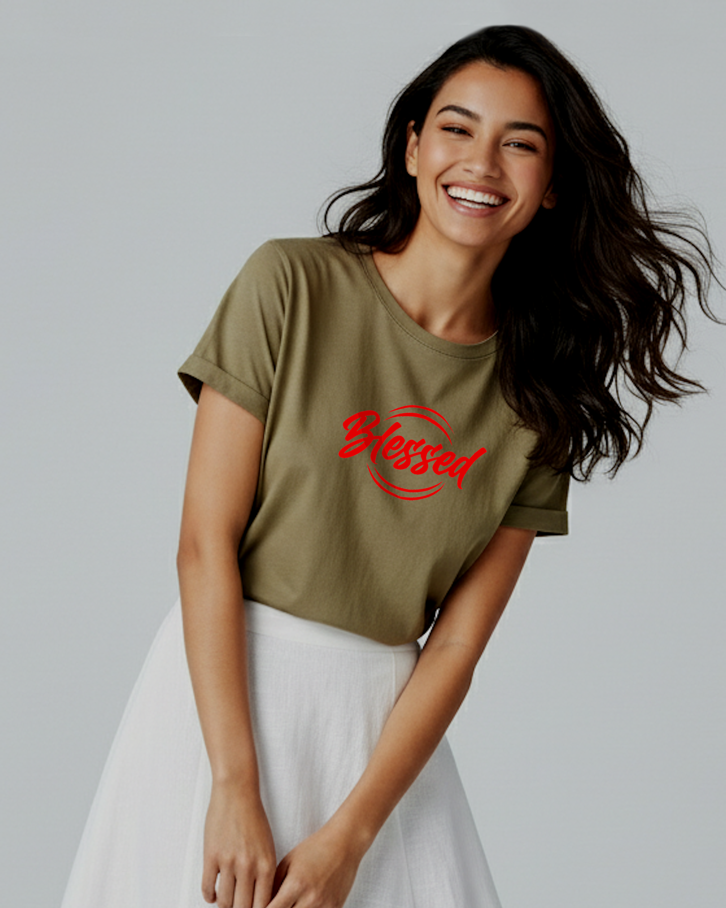 Woman wearing a khaki short sleeve t-shirt with a red logo saying "Blessed" and a white dress against a light grey background.