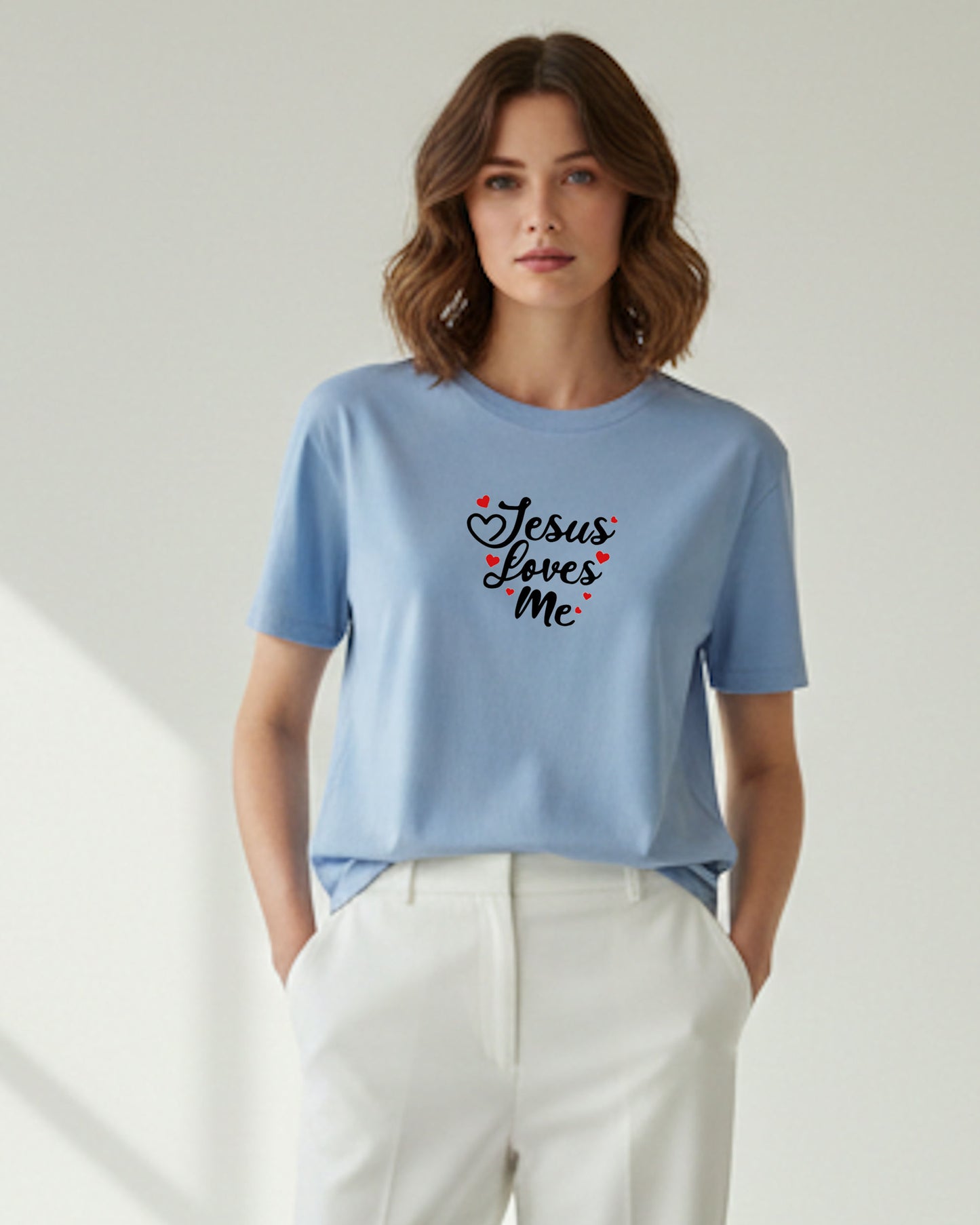Woman wearing alight blue t-shirt with black 'Jesus Loves Me' text with red hearts and yellow pants on a light background