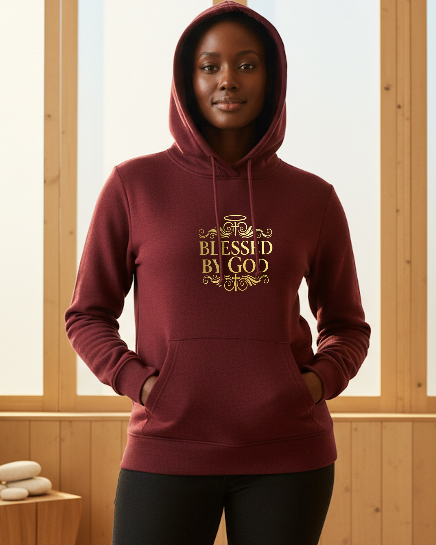 Woman wearing a maroon hoodie with 'Blessed by God' text in gold, standing indoors.