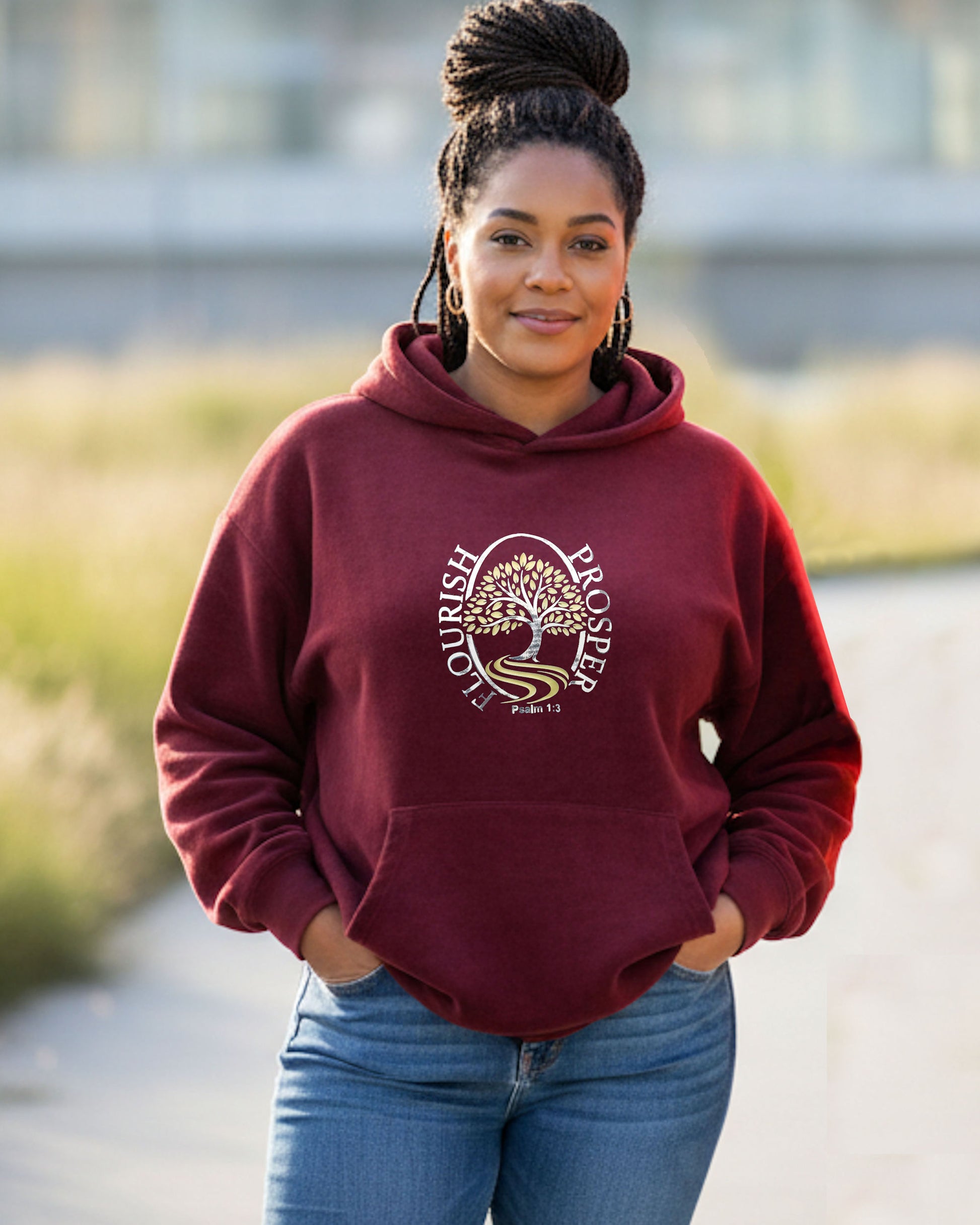 Woman outdoors wearing a maroon hoodie with a gold/silver logo with text 'Flourish Prosper Psalm 1:3'