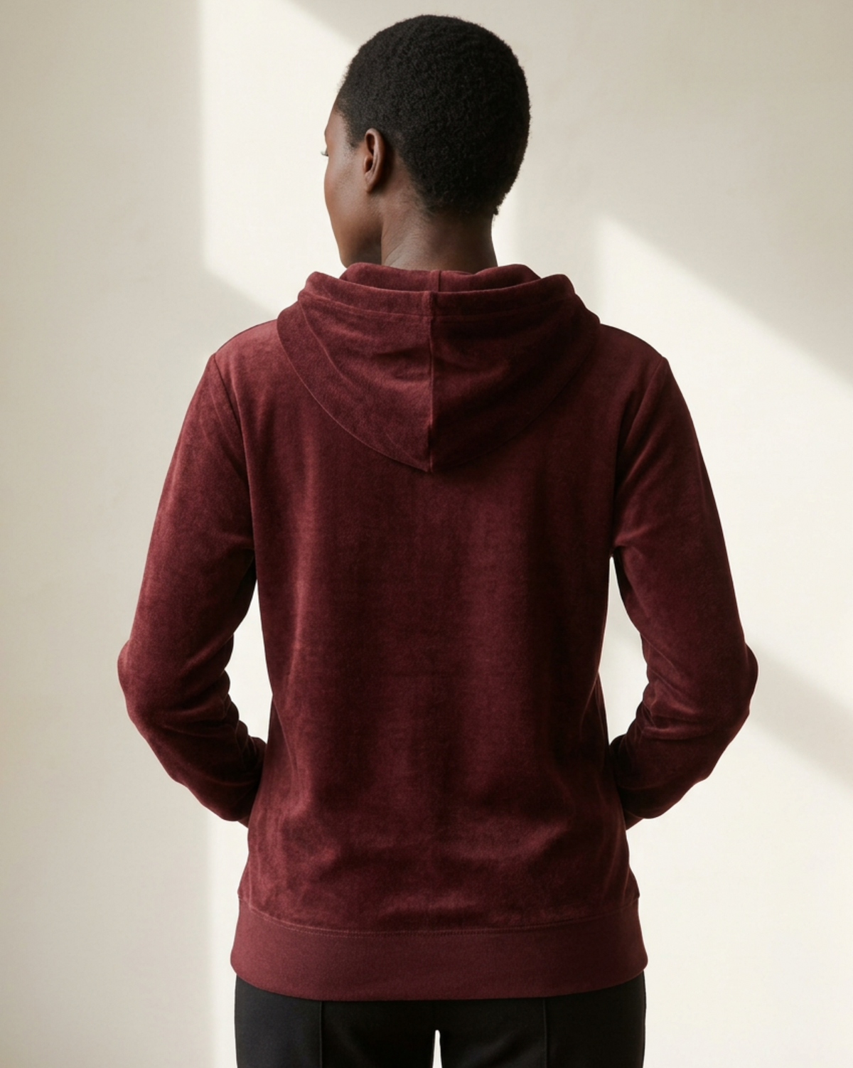 Woman wearing a maroon hoodieviewed from the rear on a neutral background