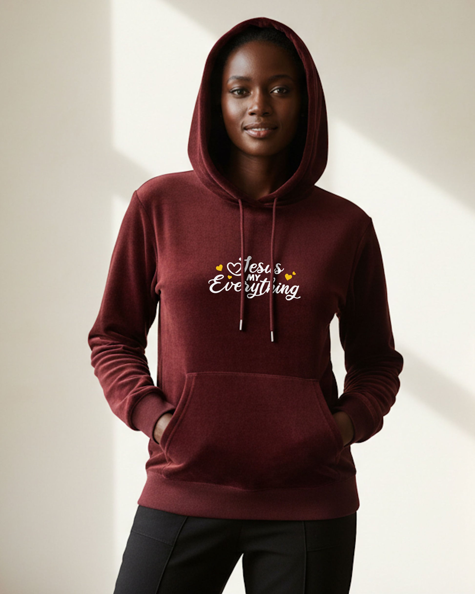 Woman wearing a maroon hoodie with 'Jesus loves everything' white text with yellow hearts on a neutral background