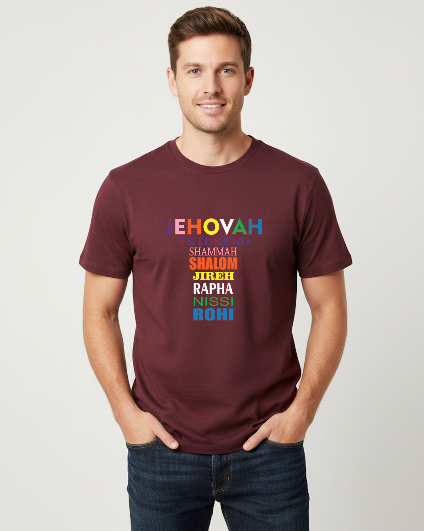 A man wearing a maroon crewneck t-shirt with a colorful text graphic on the chest, paired with dark blue jeans, standing against a light gray background.