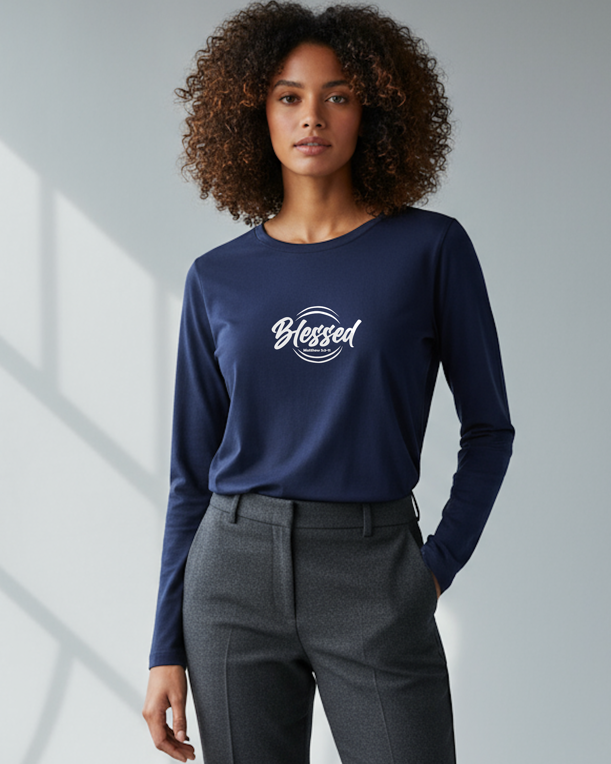 Woman wearing a navy blue long-sleeve shirt with 'Blessed' white text, standing against a gray background wall.