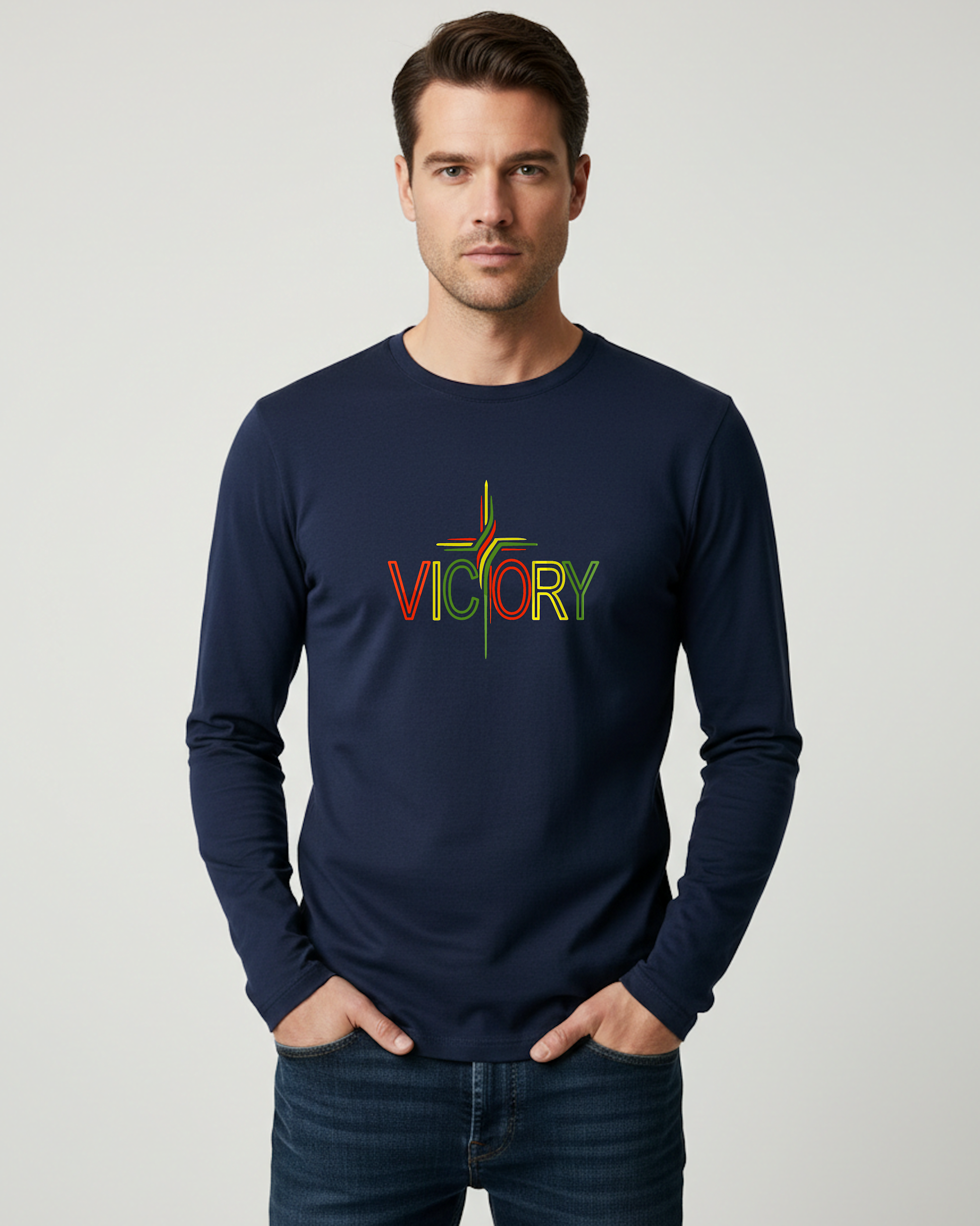 A man wearing a navy blue long-sleeve t-shirt with a colorful 'VICTORY' graphic on the chest, paired with dark blue jeans, standing against a light gray studio background.