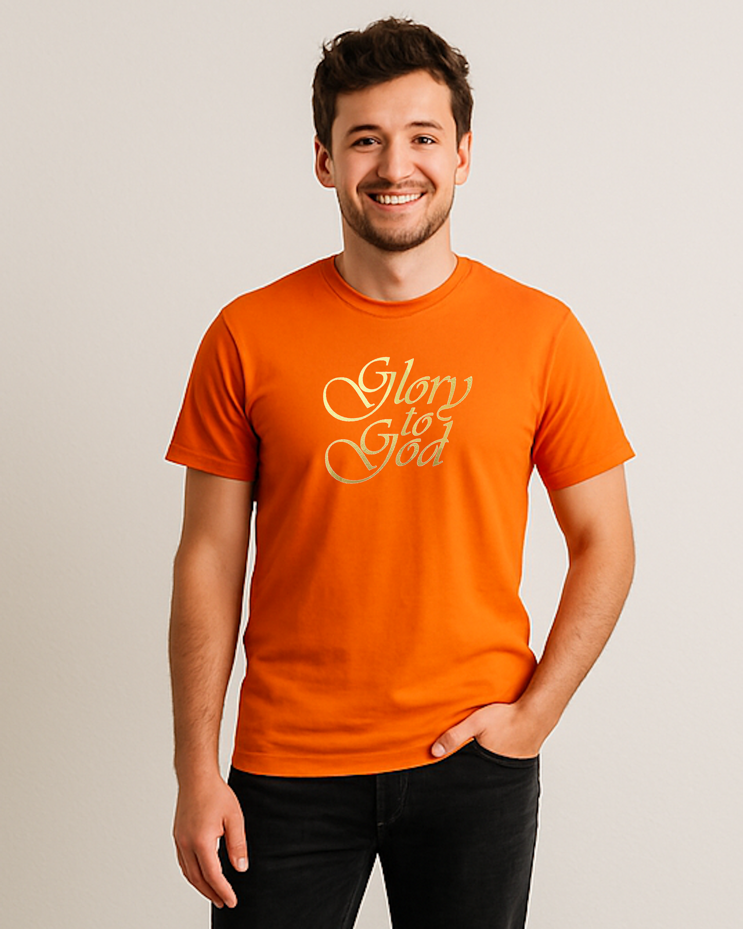 A smiling young man wearing a bright orange t-shirt with 'Glory to God' printed in metallic gold cursive across the chest, against a beige background.