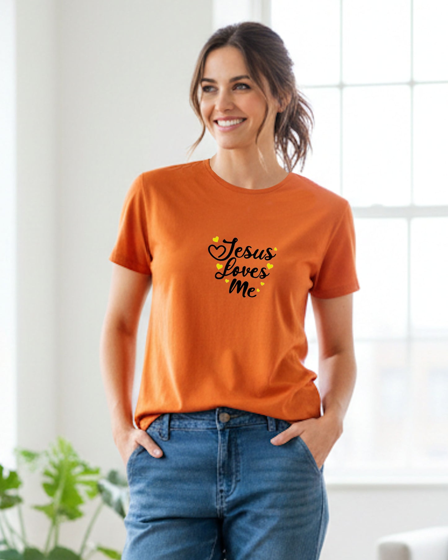 A woman a a bright indoor room wearing an orange t-shirt with 'black Jesus Loves Me' text and yellow hearts