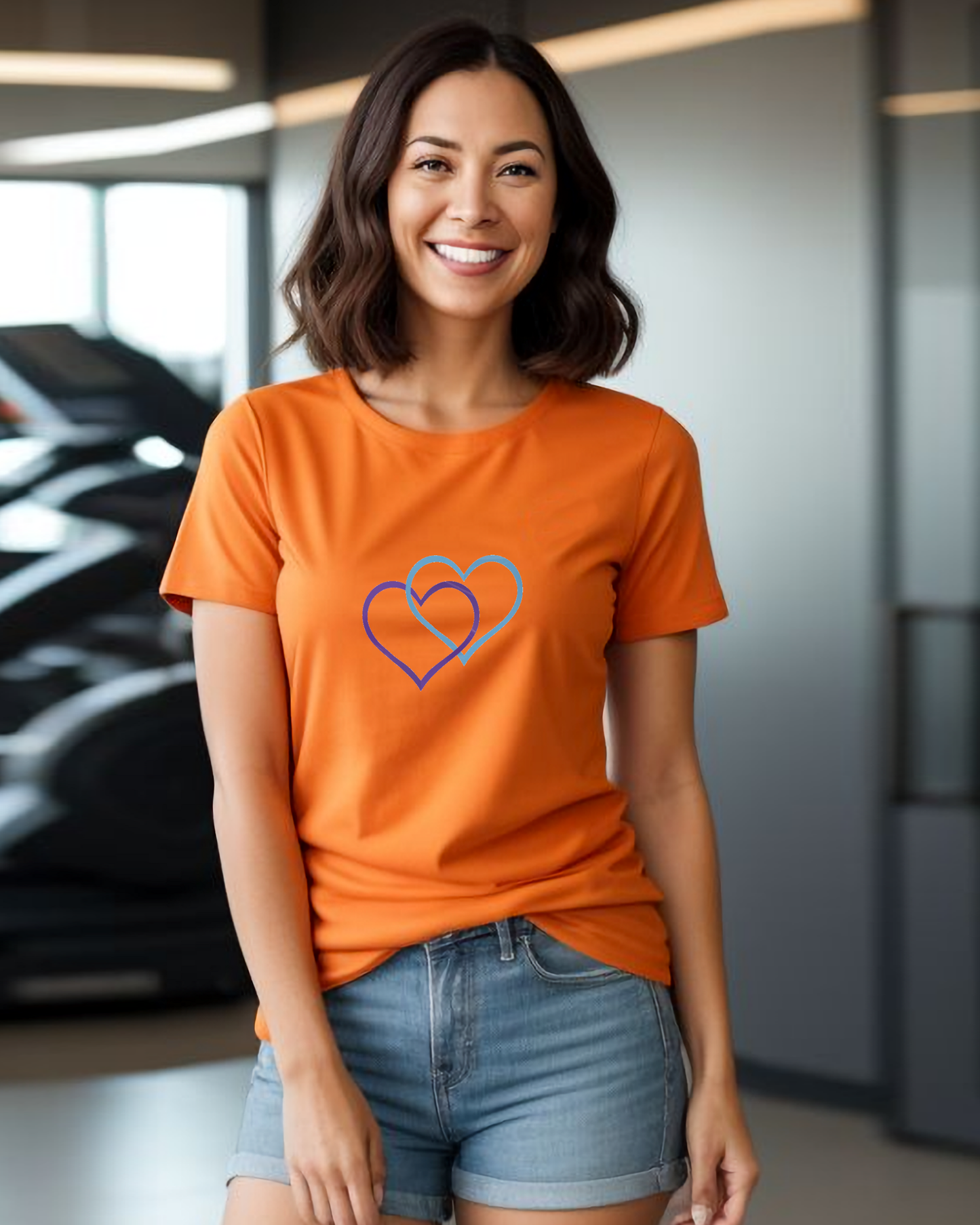 A woman in a lounge wearing an orange t-shirt with a Heavenly Dreamwear logo comprised of a purple and blue inter-twinned hearts.