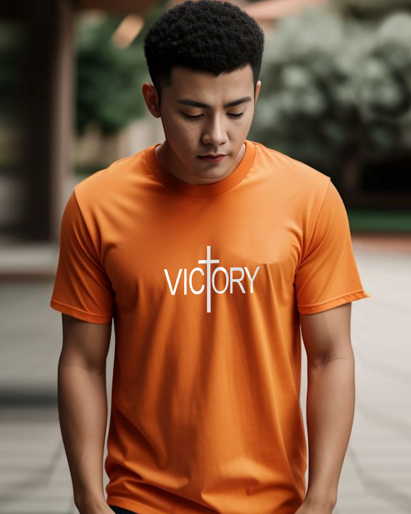 A man wearing an orange t-shirt with a white Heavenly Dreamwear "Victory" logo printed on the front, standing in a garden.
