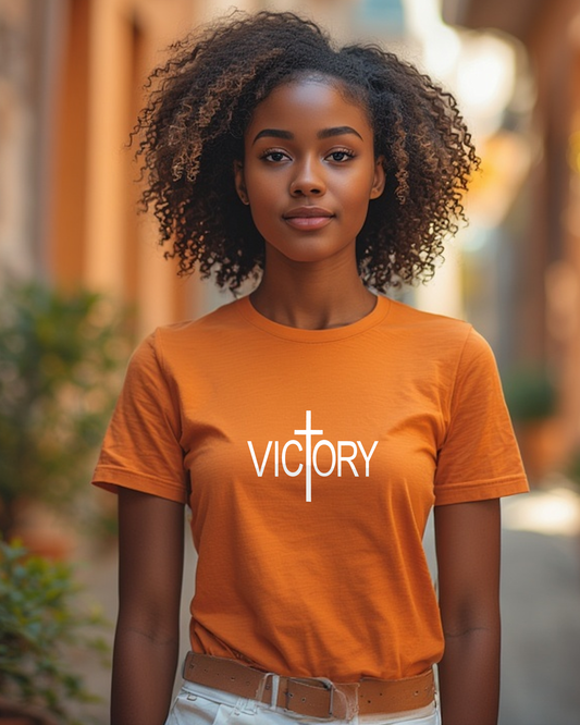 Woman wearing an orange t-shirt with a white 'VICTORY' logo outdoors