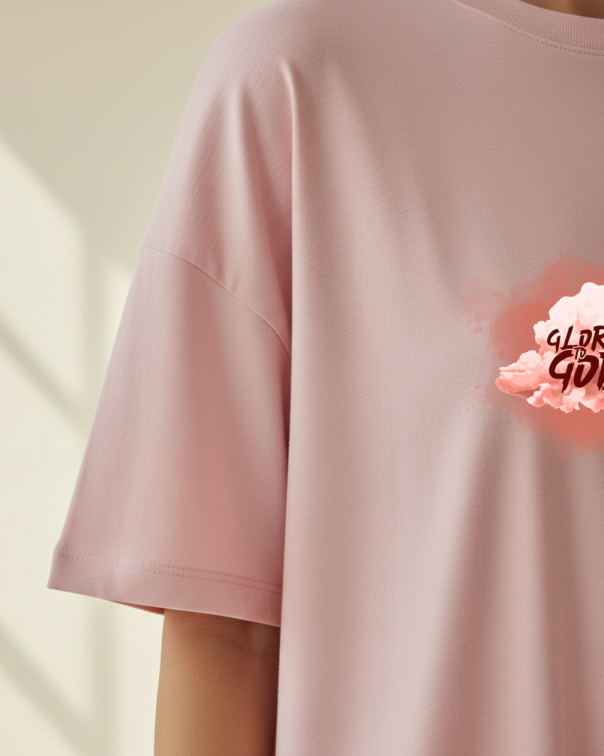 A closeup top front sleeve view of a woman wearing a pink t-shirt dress with a graphic Glory to God text in a cloud design in a bright sunlit room.
