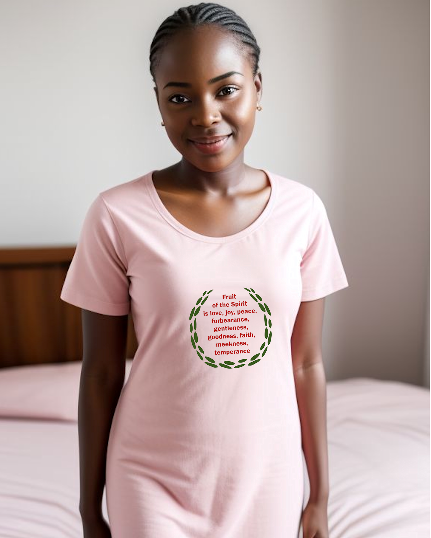 A woman in a bedroom wearing a pink t-shirt dress with a logo stating the fruit of the Holy Spirit in red text surrounded by green leaves.