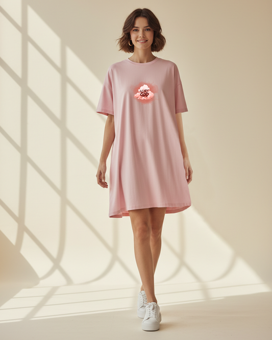 Woman wearing a pink t-shirt dress with a graphic Glory to God text in a cloud design in a bright room with sunlight filtering through.