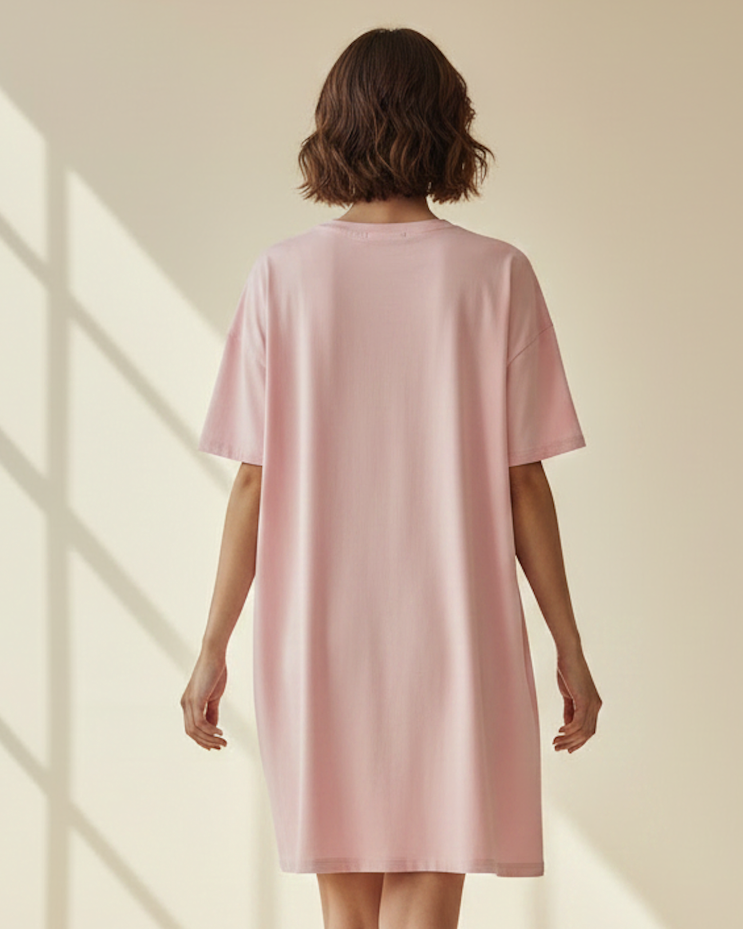 Rear view of woman wearing a pink t-shirt dress in a sunlit room.