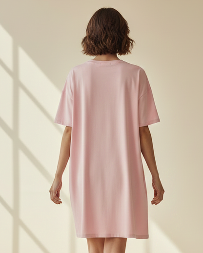 Rear view of woman wearing a pink t-shirt dress in a sunlit room.
