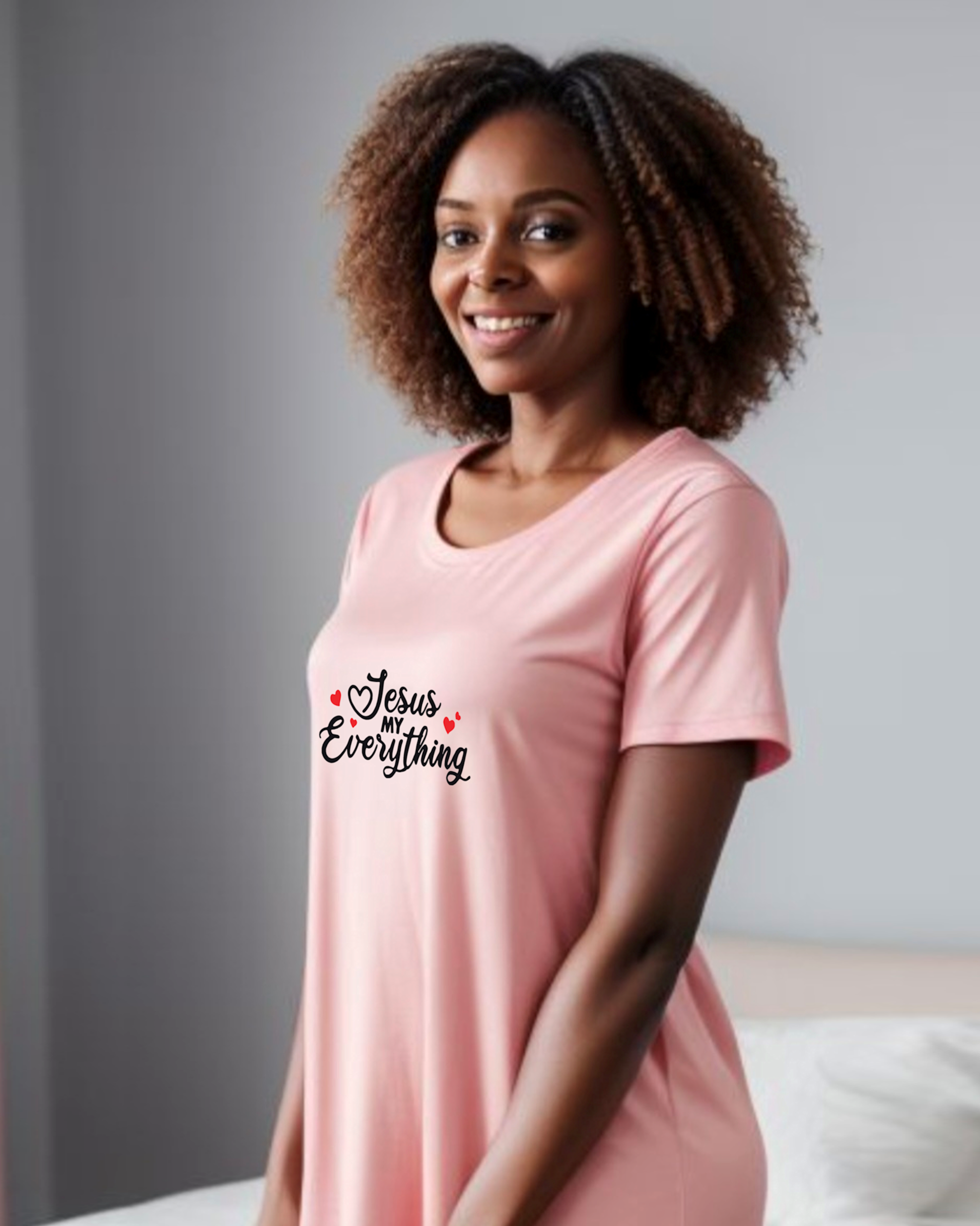 Woman wearing a pink Heavenly Dreamwear t-shirt dress in a bedroom with a black text logo "Jesus MY Everything" with 4 red hearts printed on the dress.