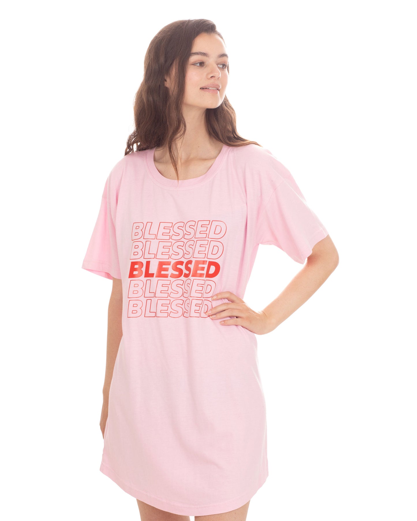 A woman modeling a light pink oversized t-shirt dress with a graphic text print reading 'BLESSED' in red on the front, set against a plain white background.
