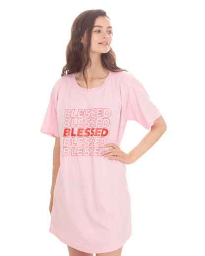 A woman modeling a light pink oversized t-shirt dress with a graphic text print reading 'BLESSED' in red on the front, set against a plain white background.