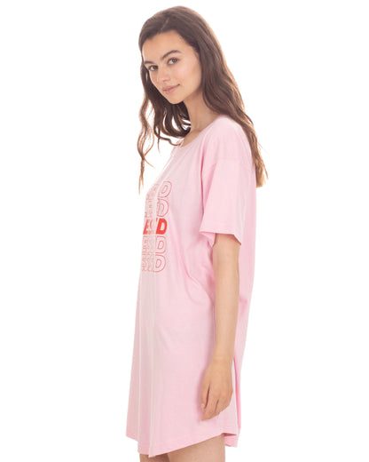 A woman wearing a light pink oversized short-sleeve t-shirt dress with a red graphic print on the front, photographed against a solid white background.