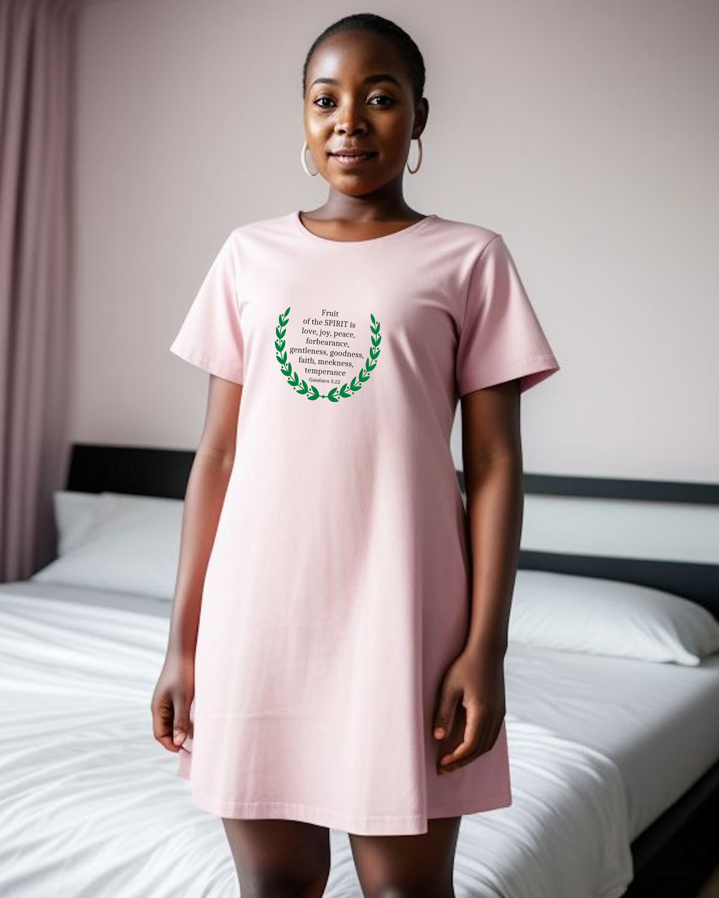 Woman wearing a pink t-shirt dress with black text and laurel wreath design in a bedroom setting