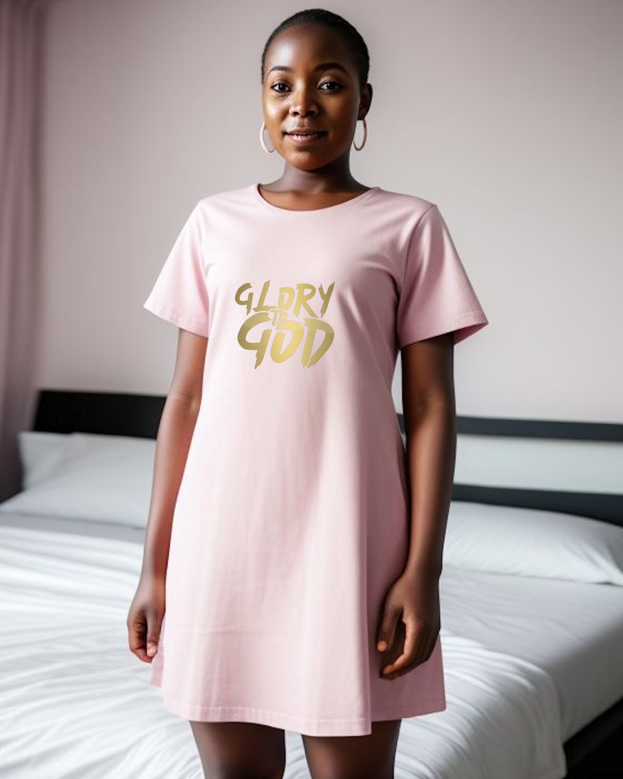 A woman in a bedroom wearing a pink cotton Heavenly Dreamwear nightdress with a gold "Glory to God" logo printed on the front.
