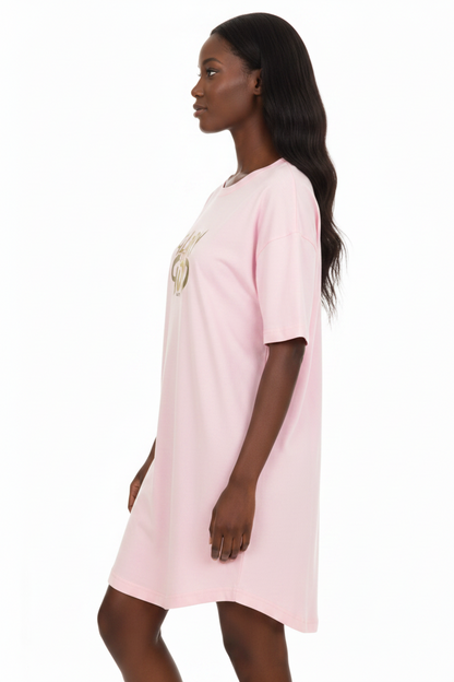 A woman wearing a light pink short-sleeve t-shirt dress with a gold graphic print on the chest, shown from a side profile against a white background.