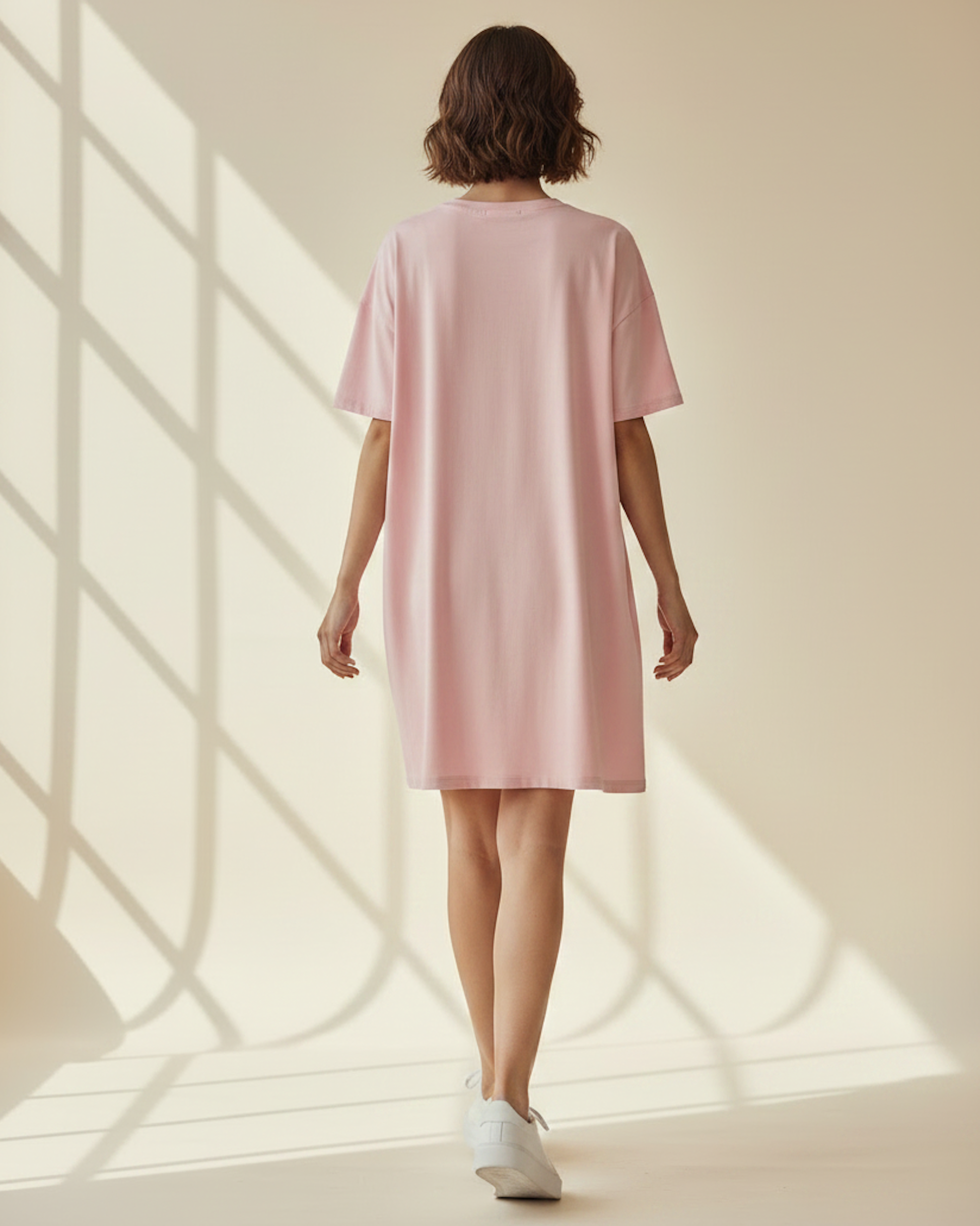A rear view of a woman wearing a pink t-shirt dress in a bright sunlit room.
