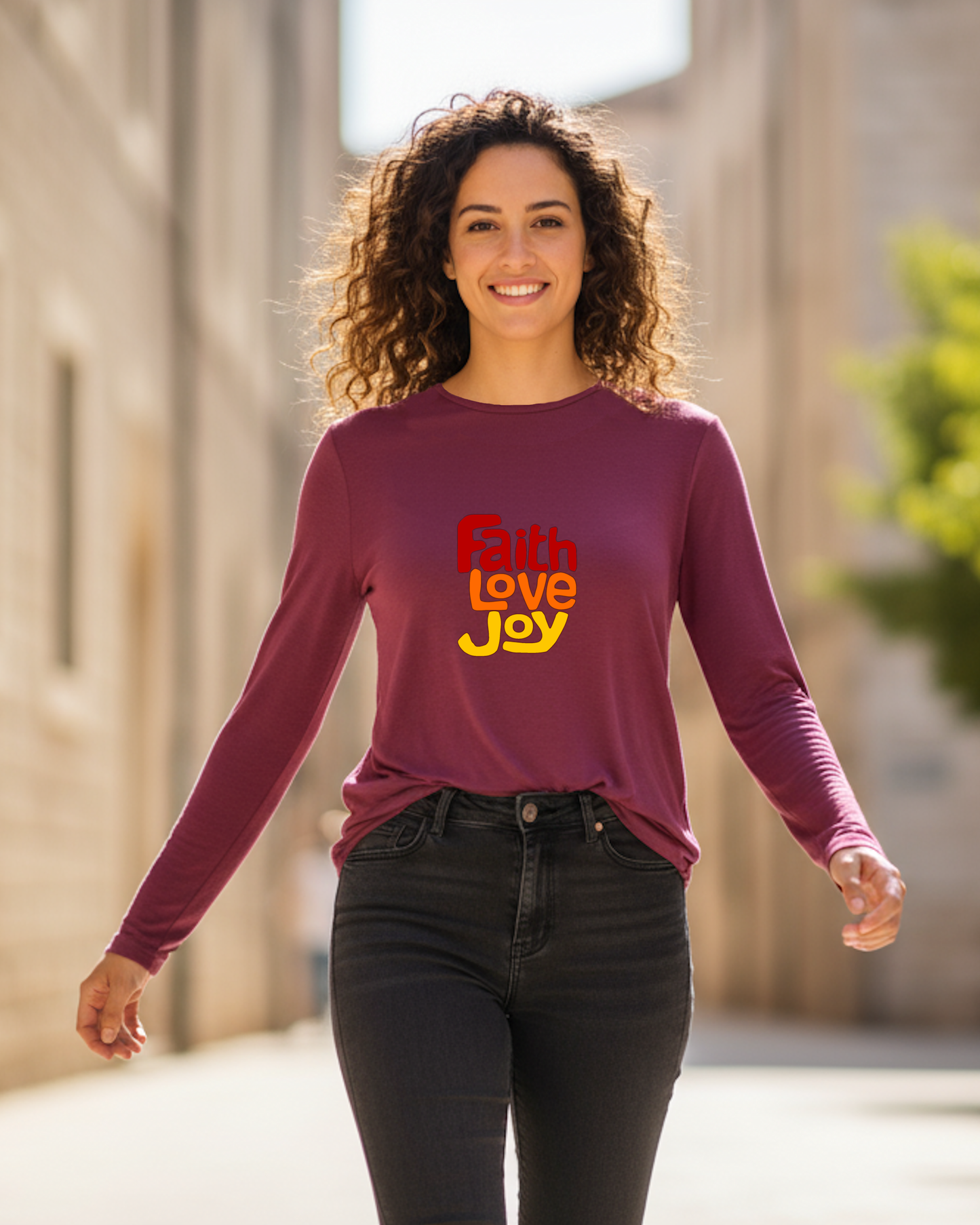 Woman wearing a purple long-sleeve t-shirt with 'Faith Love Joy' text in red, orange, and yellow outdoors.