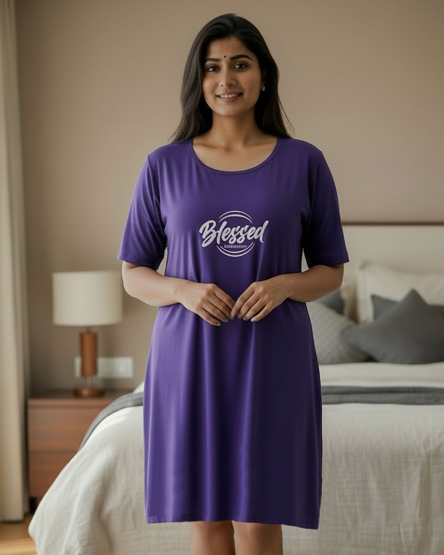 A woman wearing a purple short-sleeve nightgown with a white 'Blessed' graphic on the chest, standing in a bedroom setting.