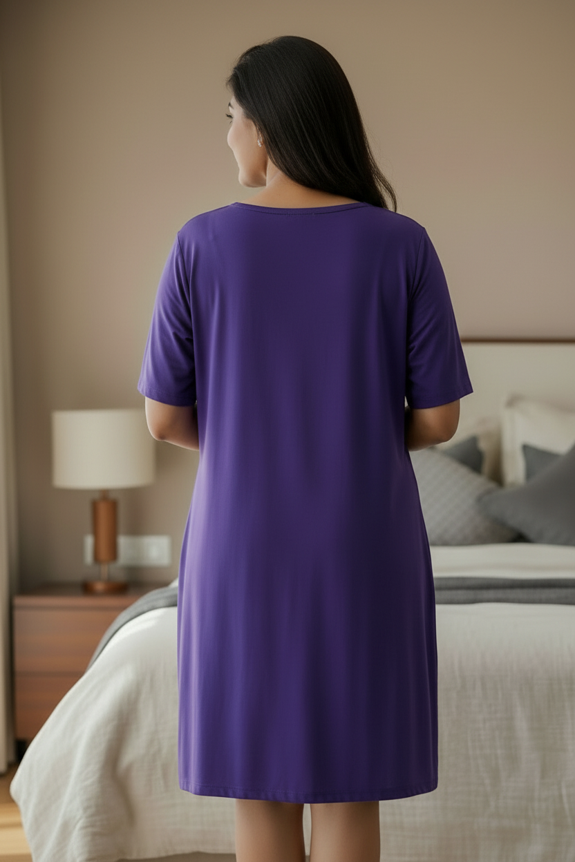 A woman viewed from behind wearing a solid purple short-sleeve shift dress in a bedroom setting.