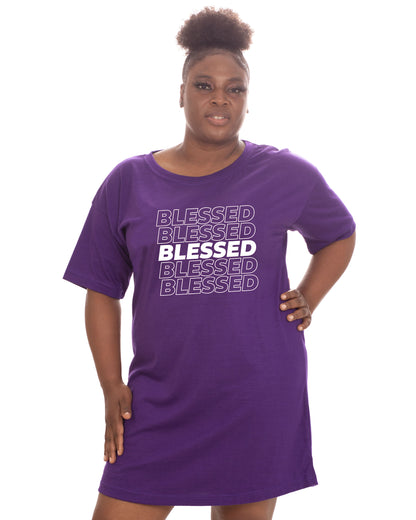 A woman modeling a purple short-sleeve t-shirt dress with 'BLESSED' printed in white text across the chest, set against a plain white background.
