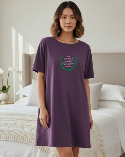 Woman wearing a purple t-shirt dress with a green design with white text in a bedroom setting
