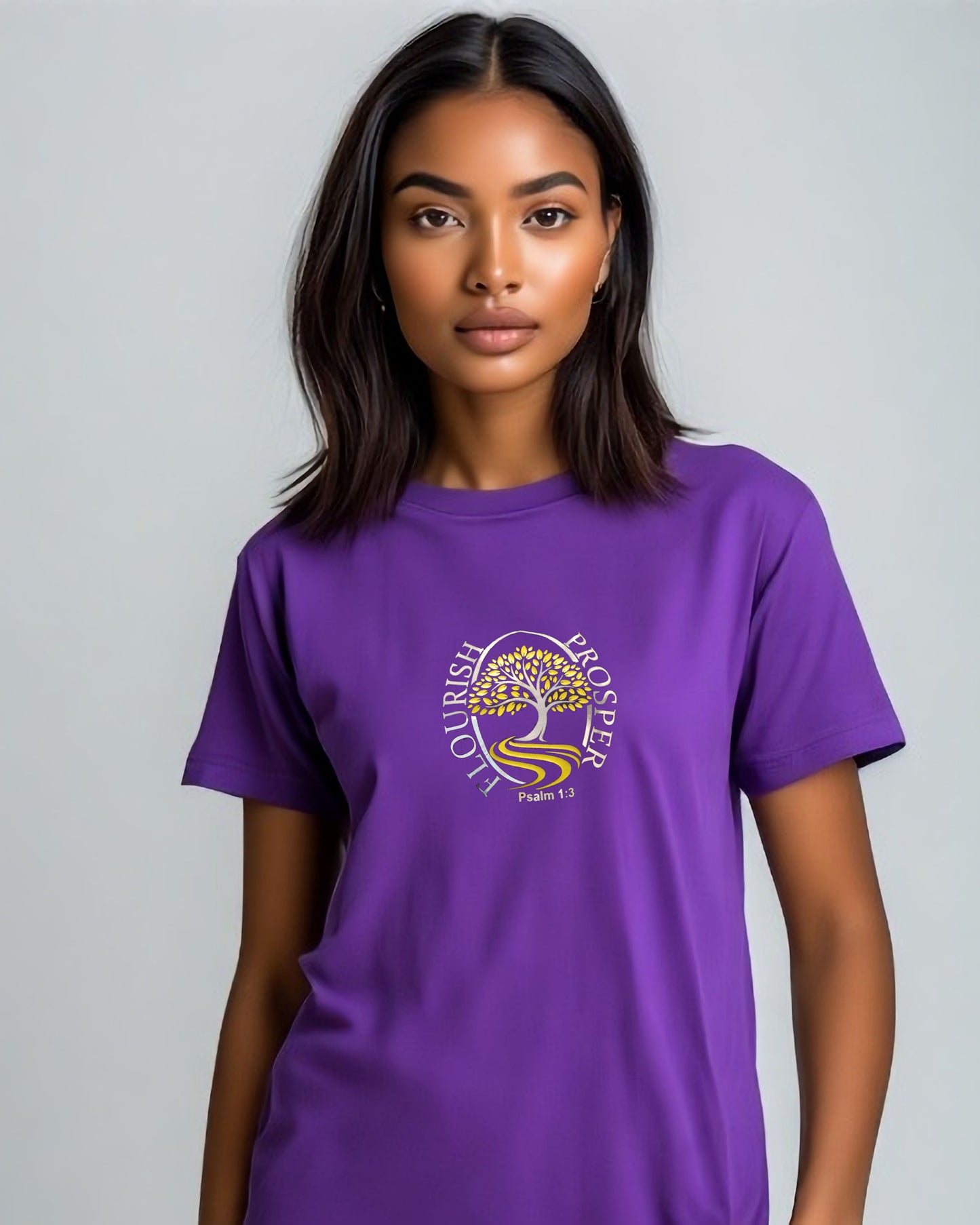 Woman wearing a purple t-shirt with a gold and silver logo (Flourish Prosper)  in a bedroom setting