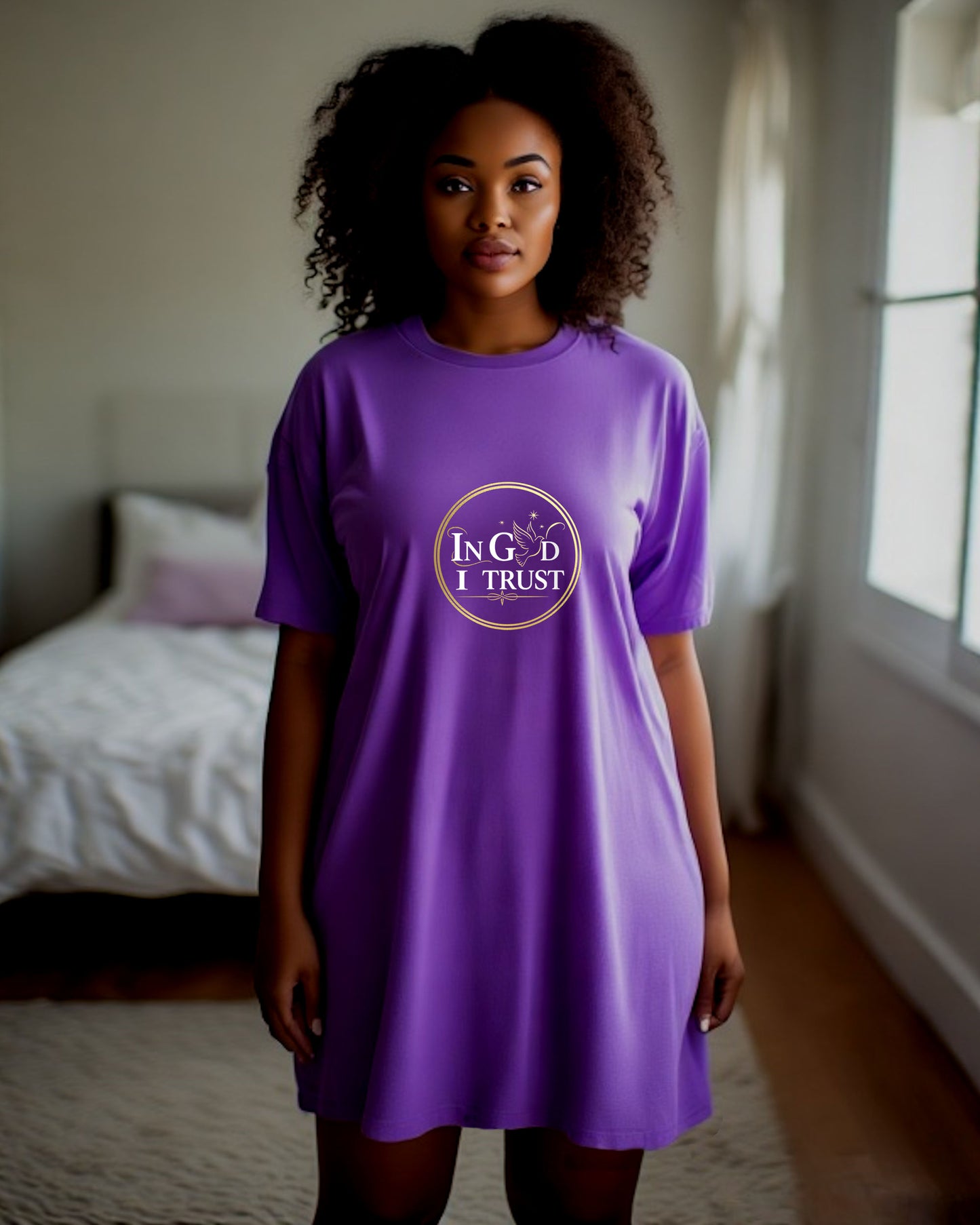 Woman wearing a purple t-shirt dress with a logo bearing text, "In God I trust" in a bedroom setting.