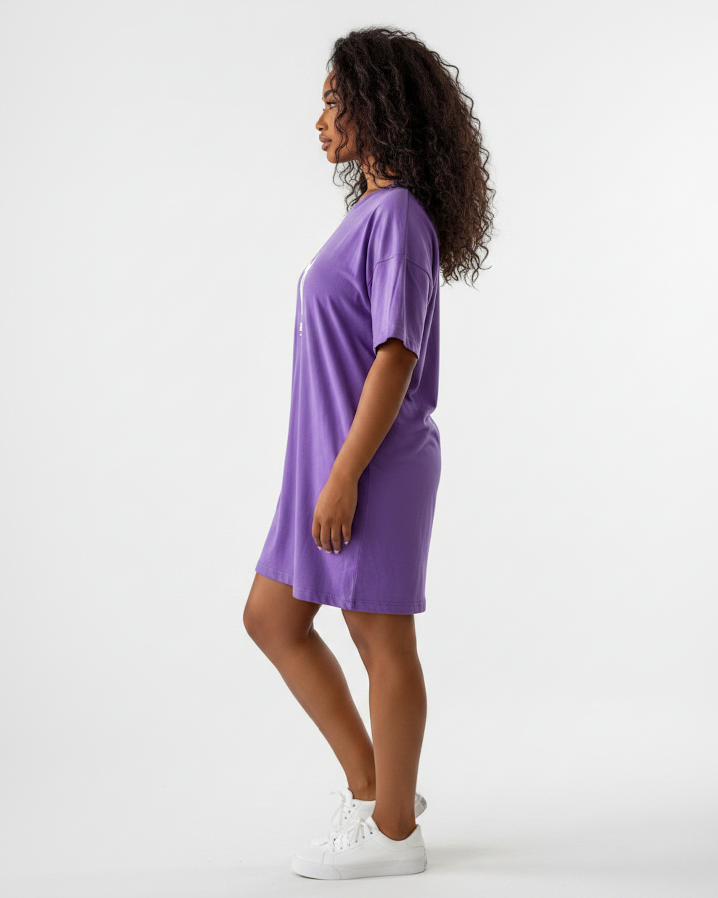 Side view of a woman wearing a purple t-shirt dress against a white background.