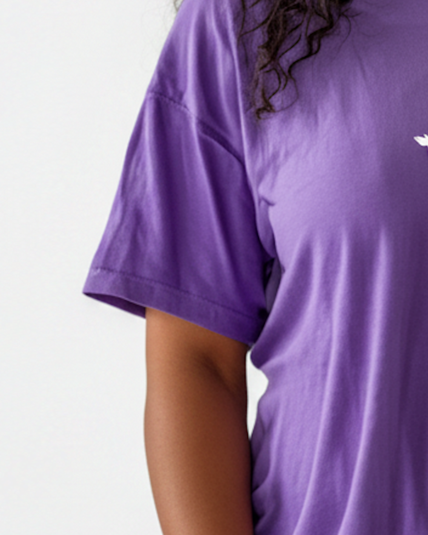 Closeup view of the sleeve of a woman wearing a purple t-shirt dress against a white background.