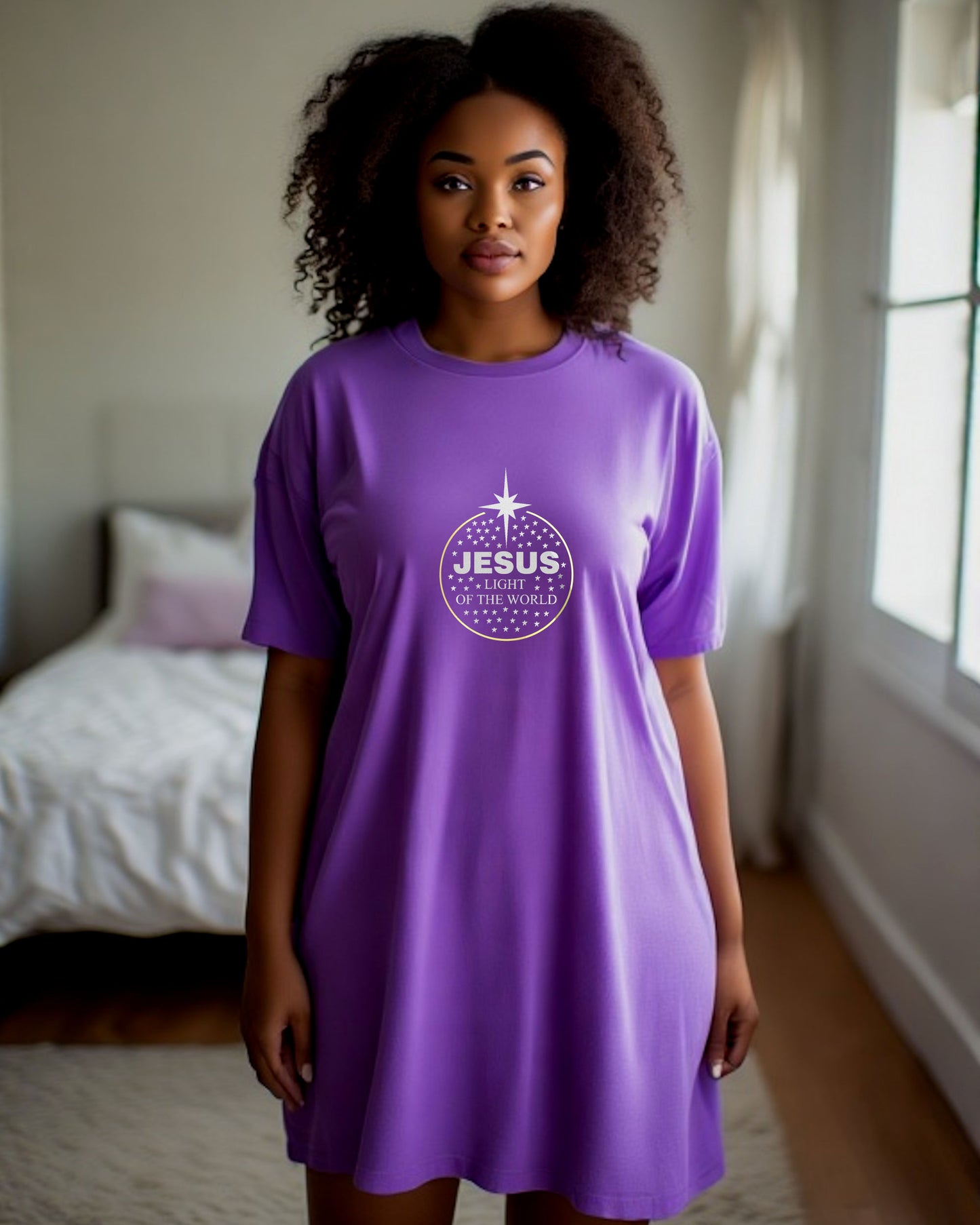 Woman wearing a purple t-shirt dress with a logo made up of silver text, 'Jesus Light of the World', silver stars, and a gold ring in a bedroom setting