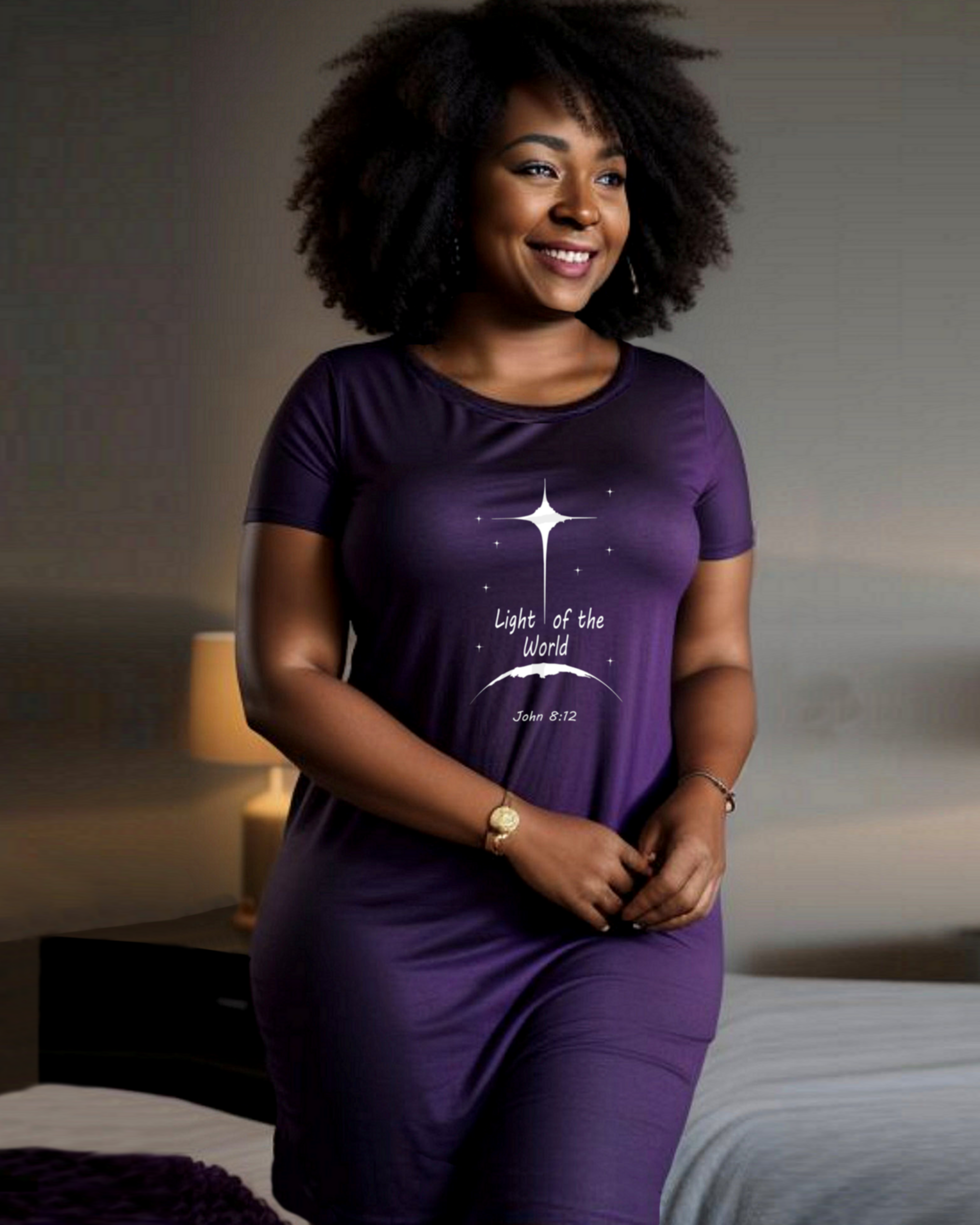 A woman standing in a bedroom wearing a purple t-shirt dress with a white Heavenly Dreamwear logo that says "Light of the World" printed on the front.