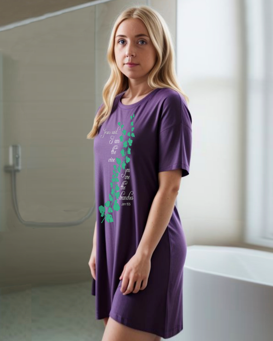 A woman wearing a purple t-shirt dress with an elaborate green vine branch with the text, "Jesus said: I am the vine you are the branches" printed in white text on either side.