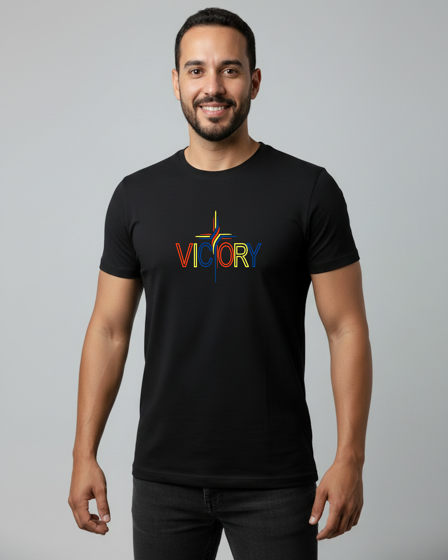 A man wearing a black short-sleeve t-shirt with a colorful 'VICTORY' graphic on the chest, standing against a solid gray studio background.