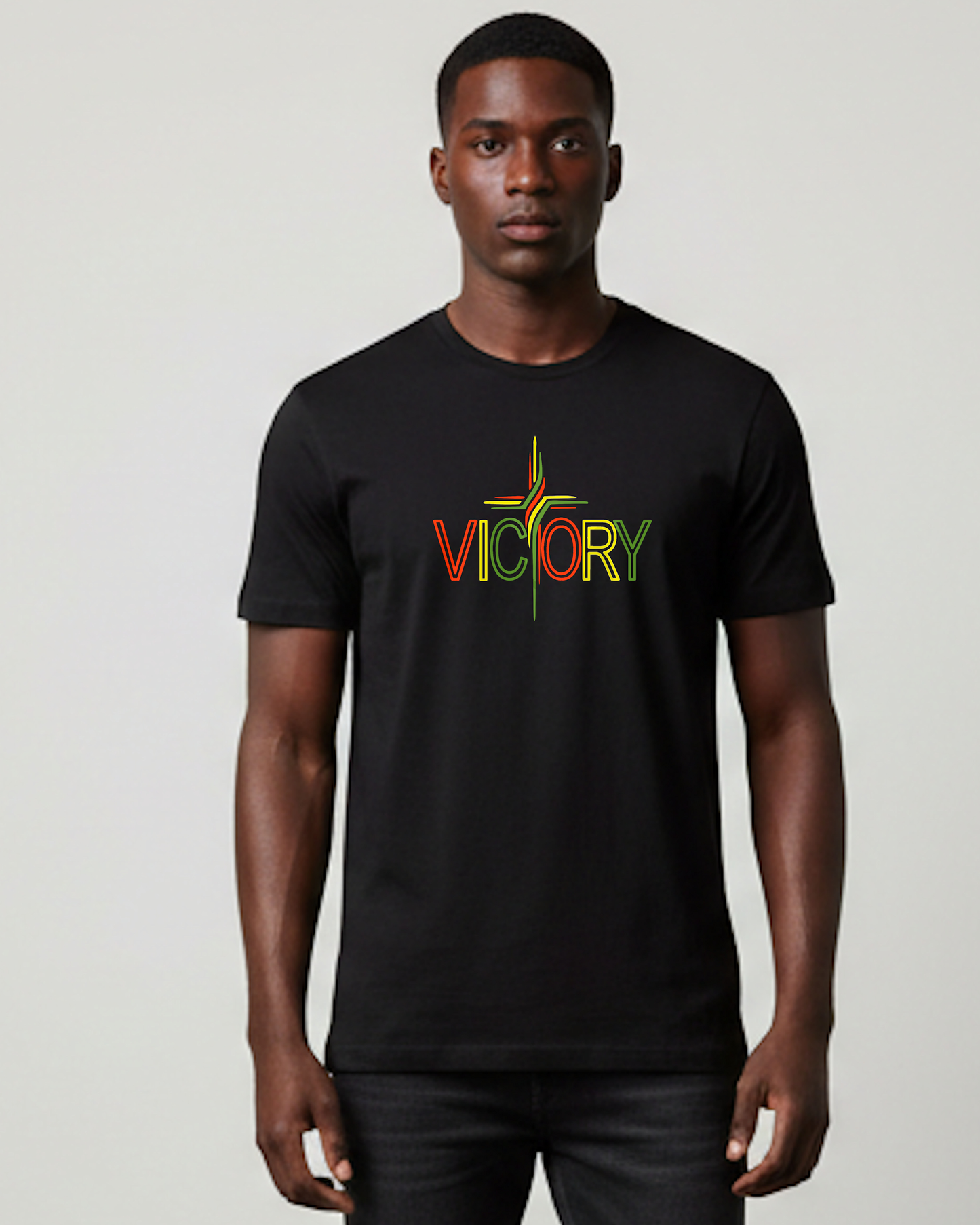 A man wearing a black t-shirt with a red, yellow, and green Heavenly Dreamwear "Victory" logo printed on the front. he 'T' is made in the shape of a stylish cross, all against a grey background.