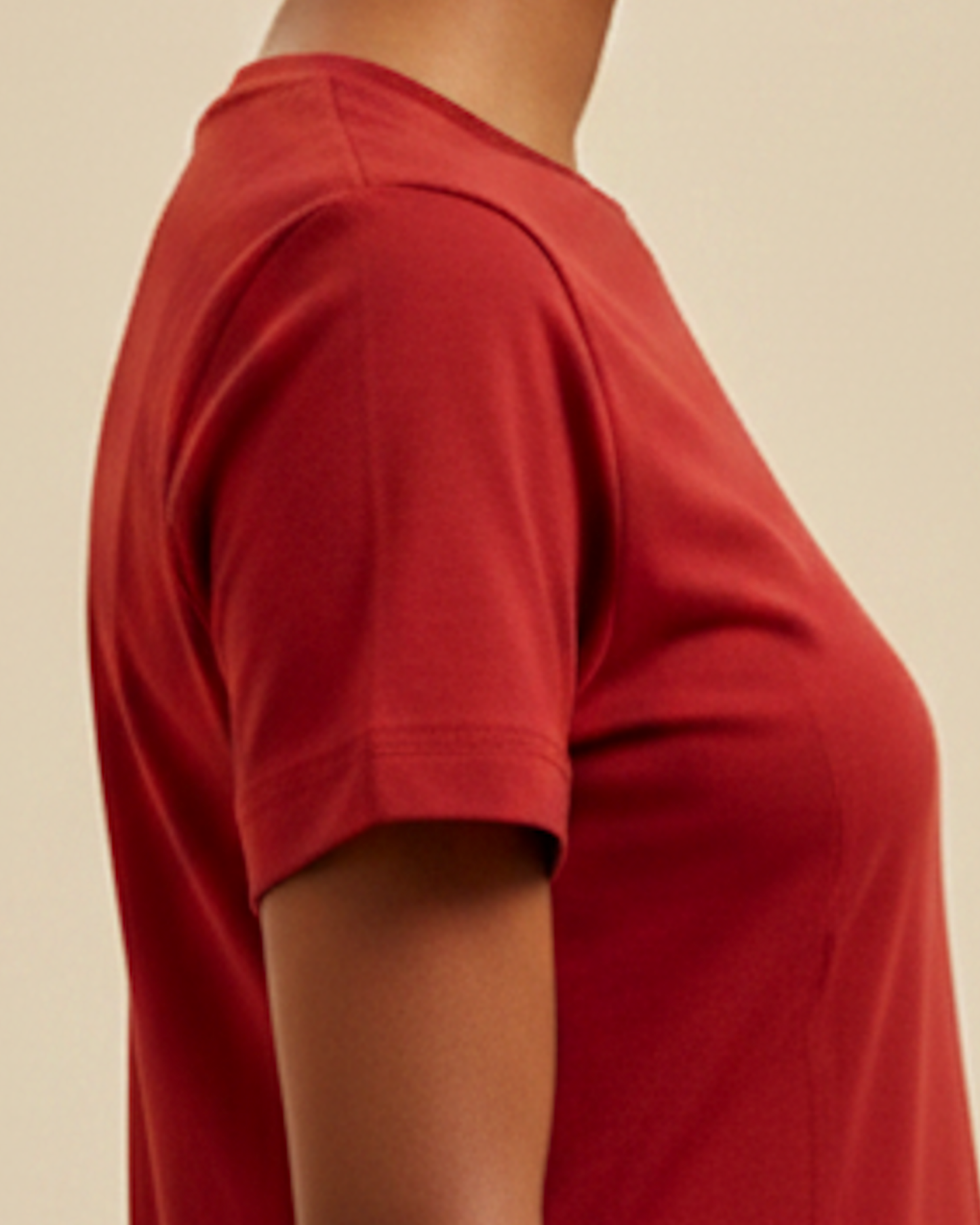 Closeup of the sleeve of a red t-shirt dress worn by a woman against a beige background.