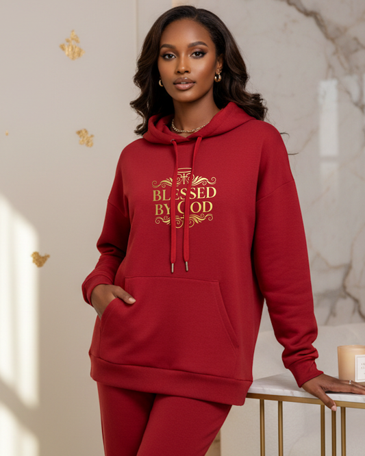 Woman wearing a red hoodie with 'Blessed by God' text in gold, standing indoors.