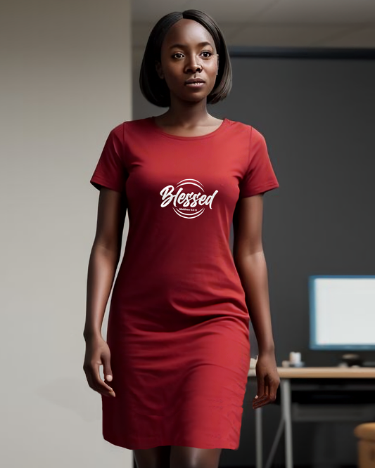 A woman in an office wearing a red Heavenly Dreamwear t-shirt dress with a white logo comprised of the text "Blessed" on top of a broken double circle with a biblical scripture reference beneath the text.